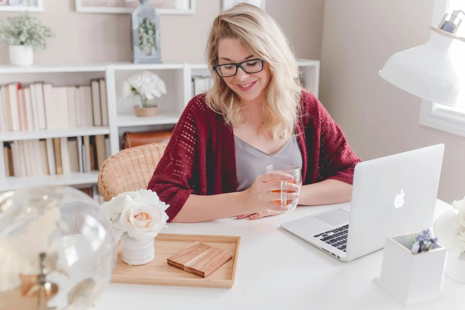 A smiling woman with a cup of tea at her desk at home, working on a laptop