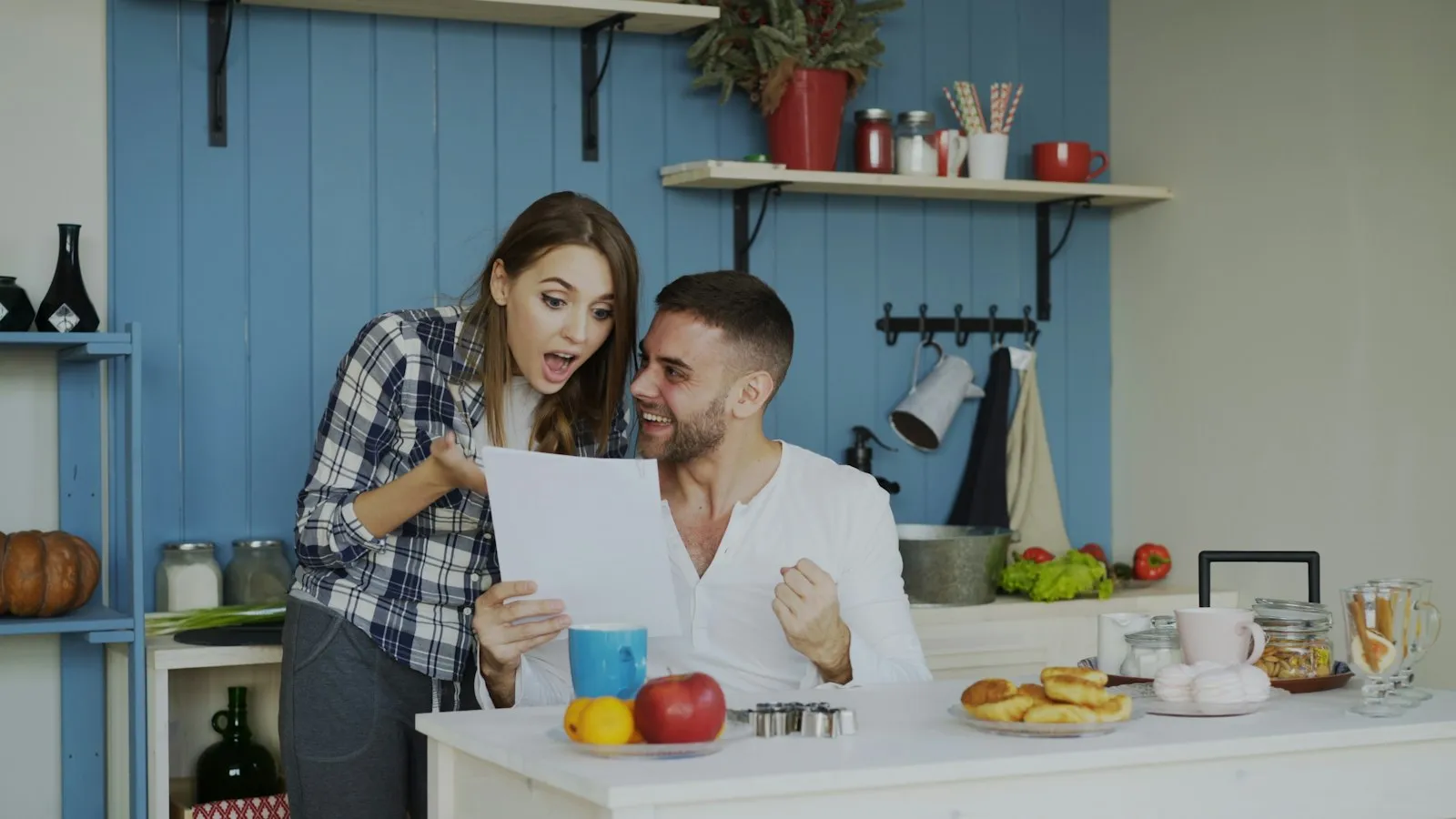 A young couple in their kitchen, delighted as they read a letter together over breakfast
