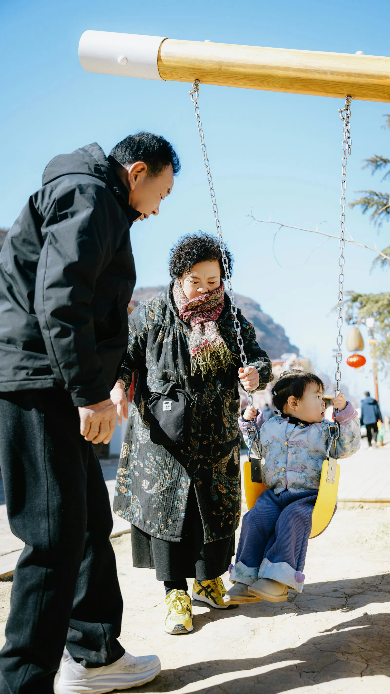 Grandparents pushing their young grandchild on a swing on a sunny day