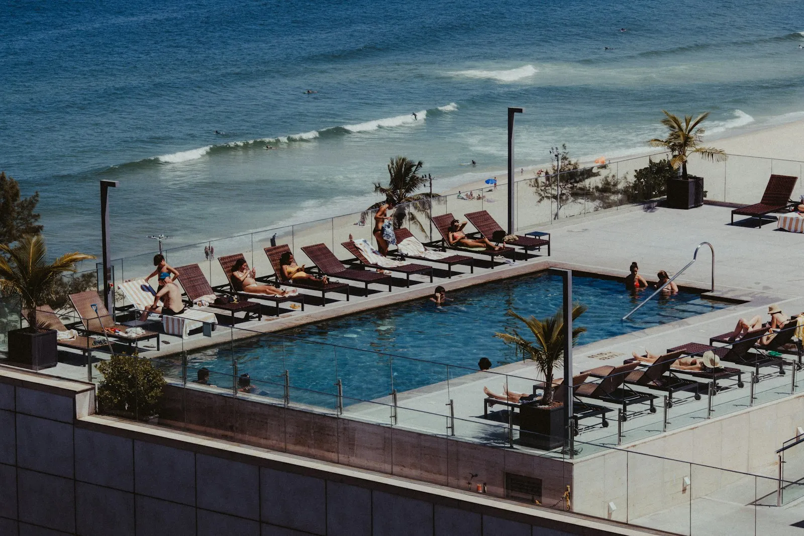 People relaxing by a rooftop pool above a sunny beach